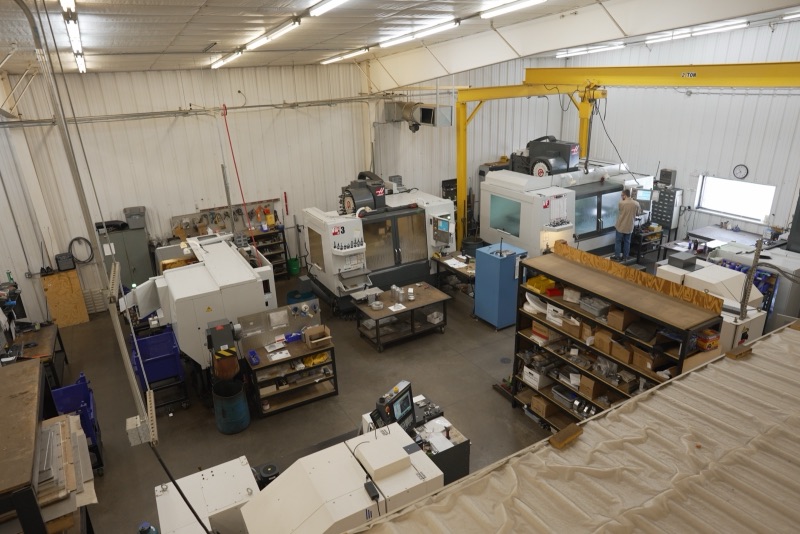 Overhead view of the HPE machine shop floor with CNC mills and a yellow gantry crane