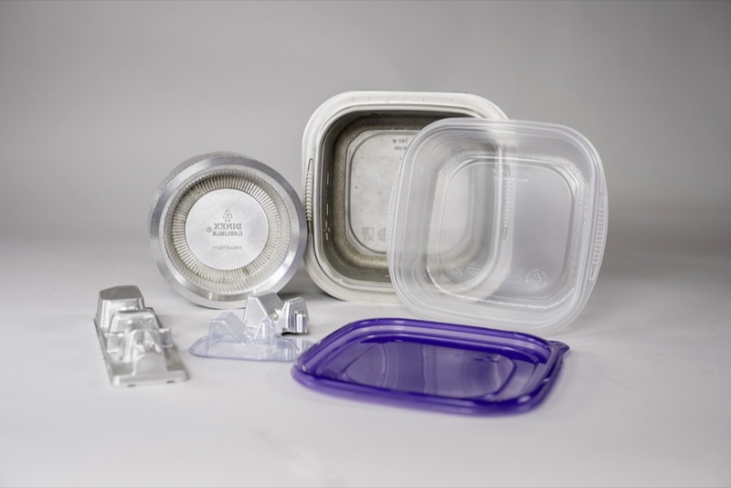 Aluminum thermoform tooling beside the clear and purple plastic trays it produces